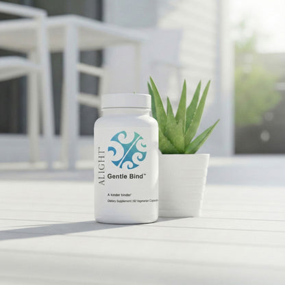 Supplement bottle labeled 'Gentle Bind' by 'ALIGHT' on a white surface with a plant in the background.