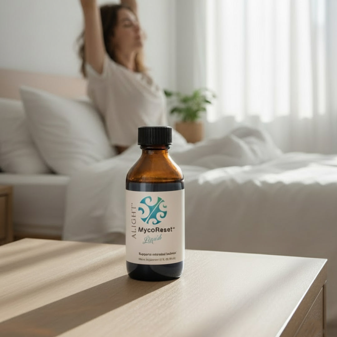 Bottle of Alight MycoReset Liquid on a table with a blurred background of a person looking "reset"  in bed.