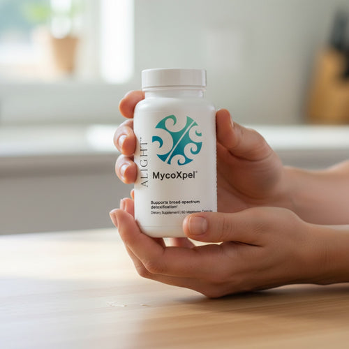 Hand holding a MycoXpel supplement bottle on a wooden surface with a blurred background