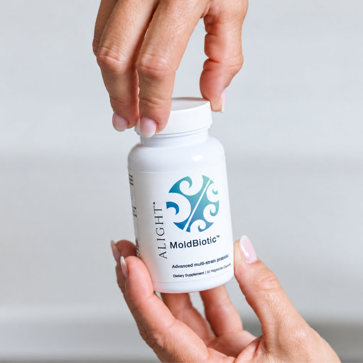 Woman holding Alight's MoldBiotic, the probiotic for mold exposure behind a white wall!